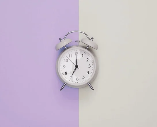 An alarm clock against a simple background which is half purple, half grey